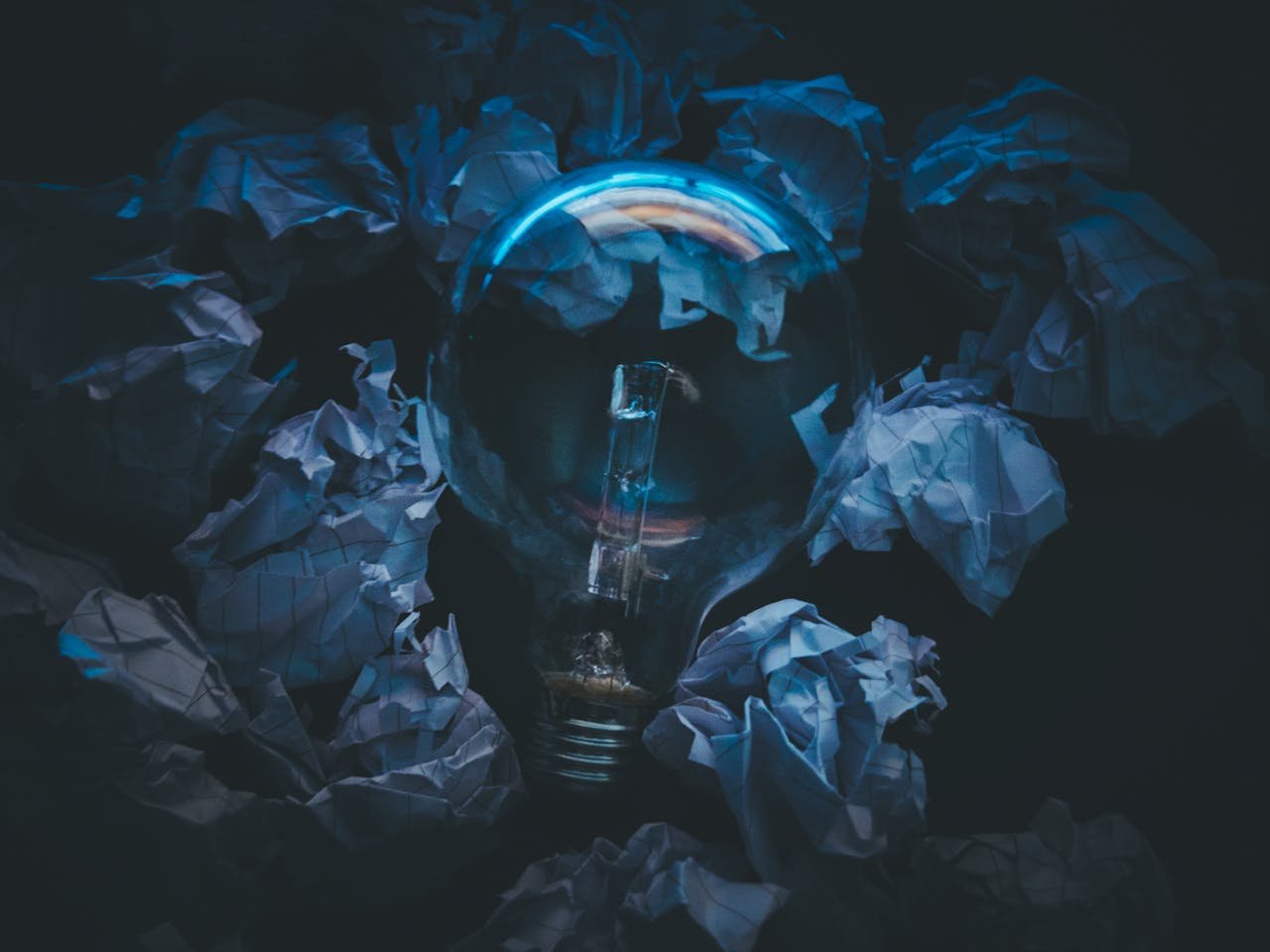 A light bulb surrounded by crumpled paper symbolizes creative ideas and innovation in a dark setting.